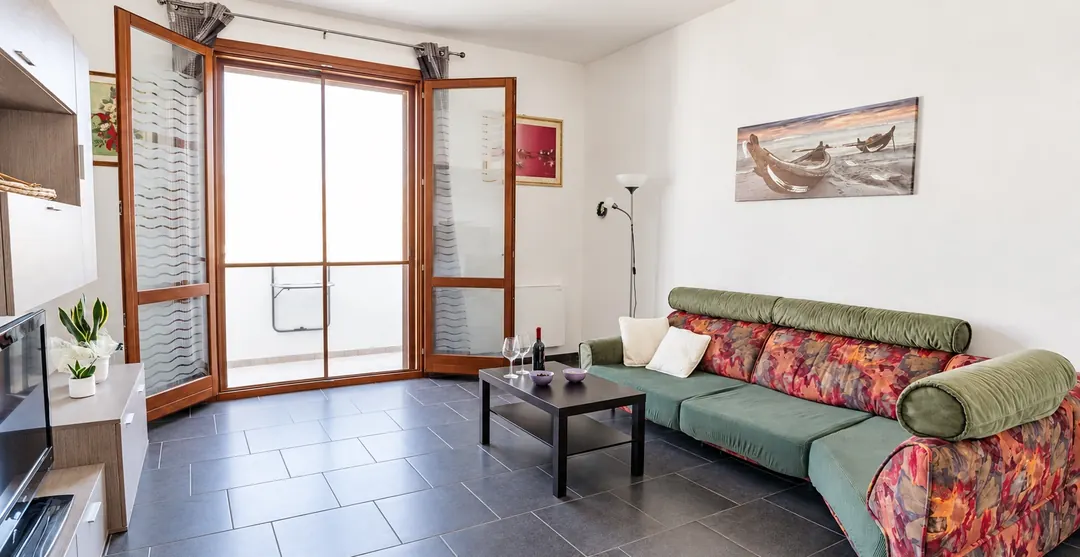 Il soggiorno: divano, tavolino e la porta-finestra aperta sul balcone